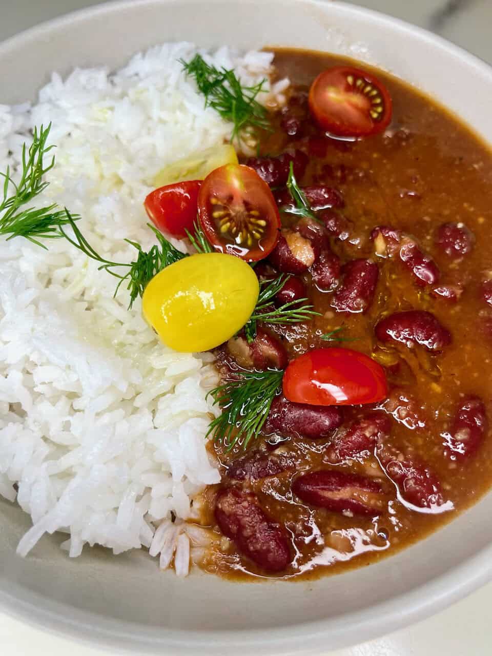 Fresh vegetable and bean chili served with white rice and garnished with cherry tomatoes and herbs.