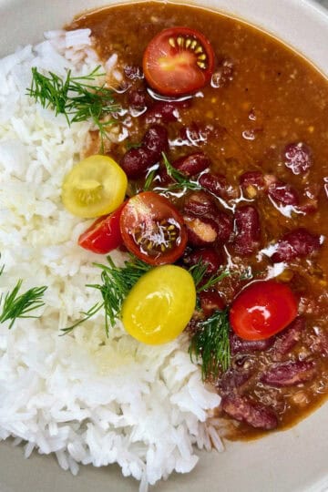Rich beef stew with cherry tomatoes, beans, and herbs served alongside fluffy white rice, perfect for a nourishing meal.