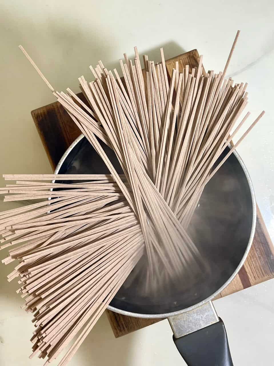 Dried wooden pasta sticks boiling in a pot on a stove.