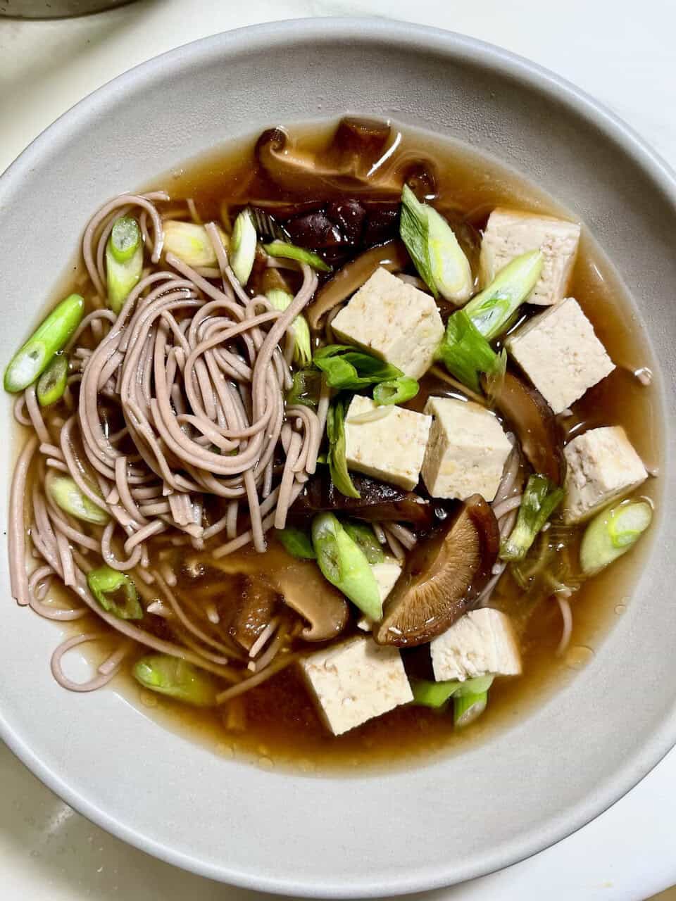 Savory mushroom and tofu noodle soup with green onions in a white bowl for healthy eating.