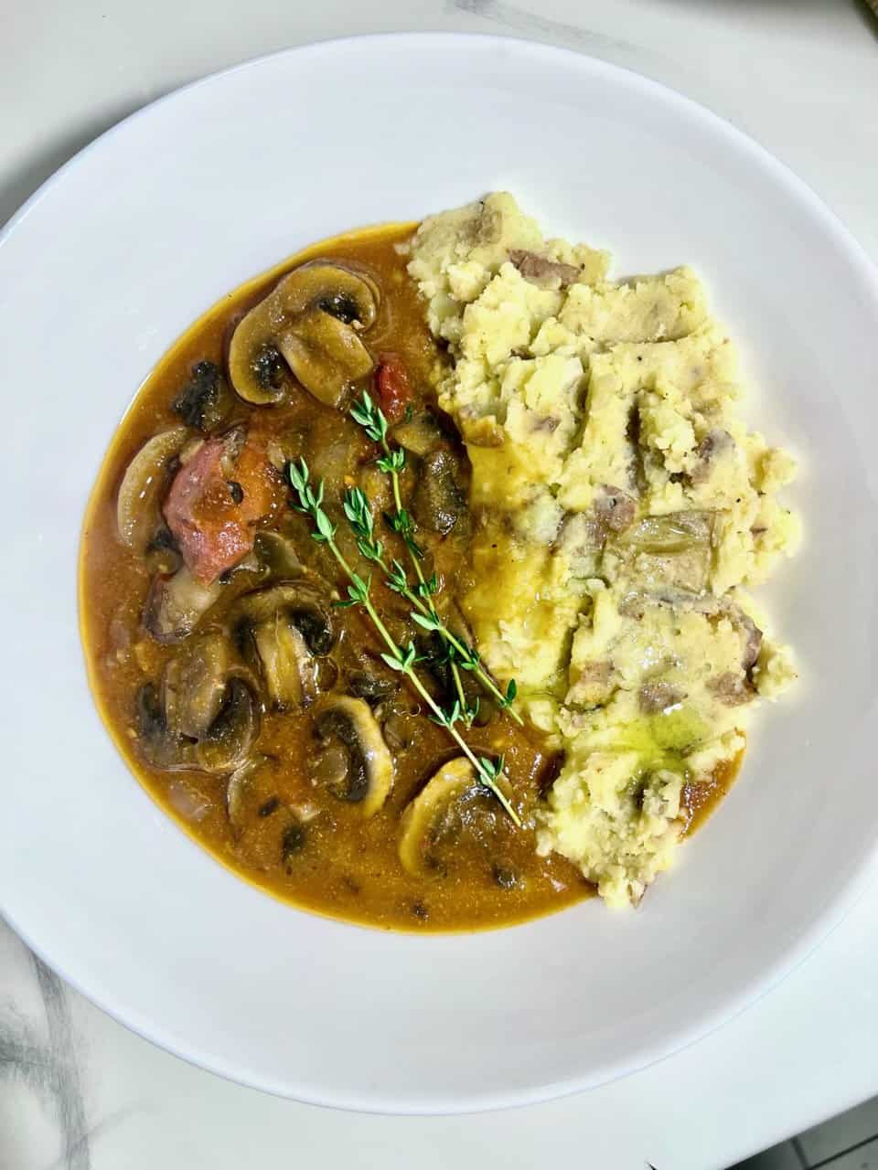 Savory mushroom gravy with mashed potatoes, served on a white plate, garnished with thyme.