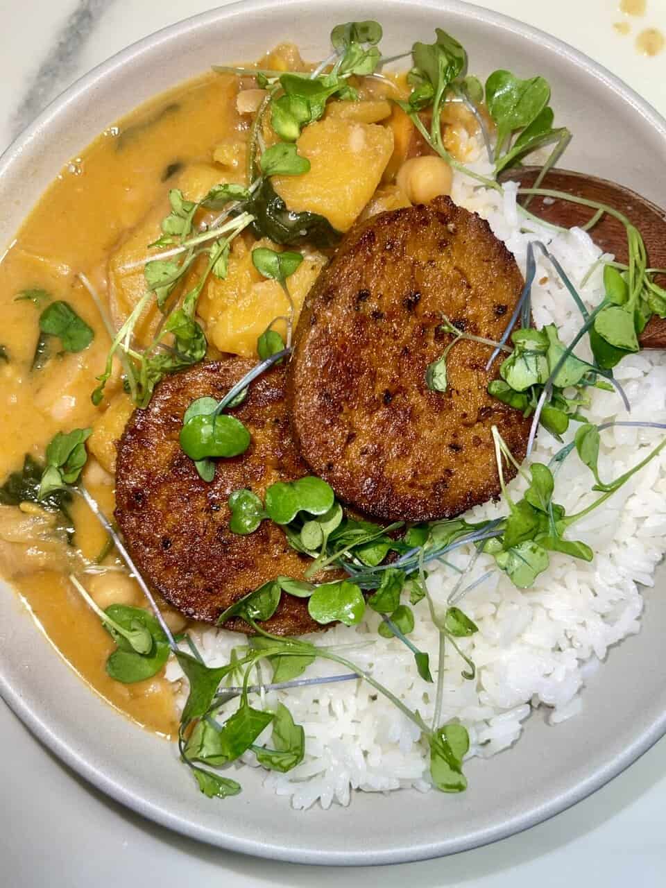 Creamy vegan curry with tofu and fresh greens served with white rice and crispy fried plantains.