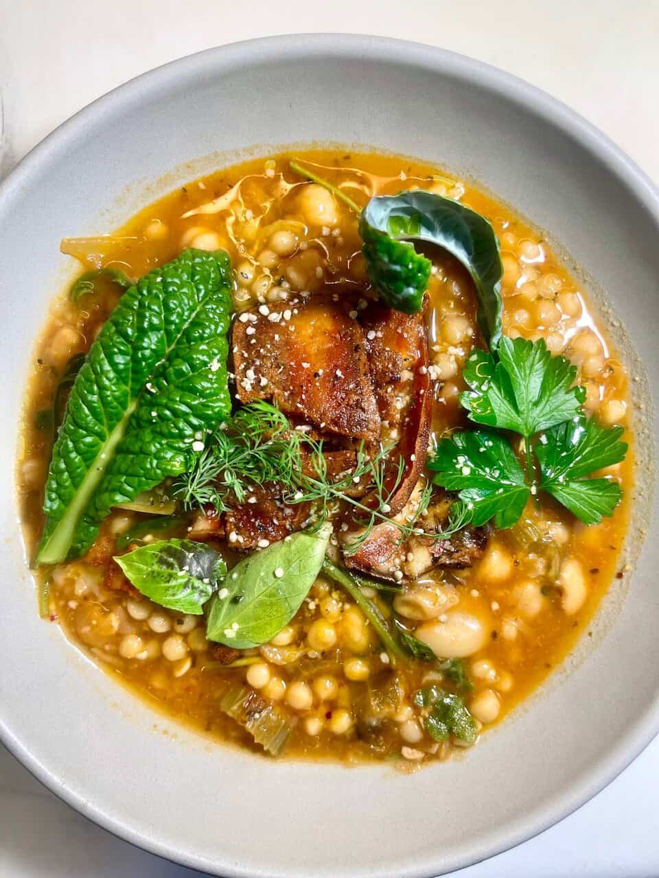 Fresh vegan soup with herbs, vegetables, and chickpeas on a white plate.
