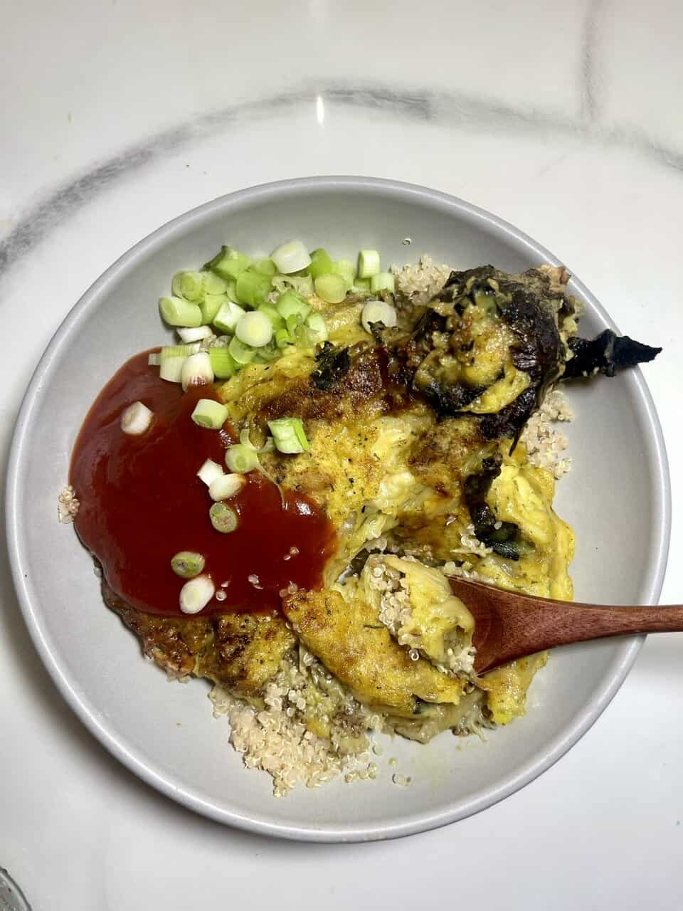 Tofu scramble with green onions and vegan ketchup over quinoa, healthy plant-based breakfast, gluten-free vegetarian meal.