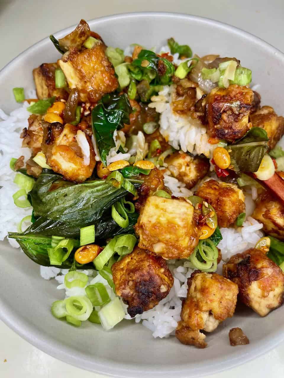 Flavorful tofu and vegetable stir-fry over rice, healthy vegan meal with green onions and fresh greens.