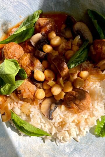 Roasted vegetable curry with rice, chickpeas, mushrooms, and fresh basil in a bowl.