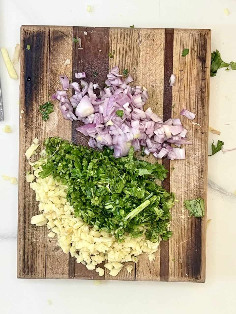 Fresh chopped onions, cilantro, and garlic on a rustic wooden cutting board for healthy cooking.