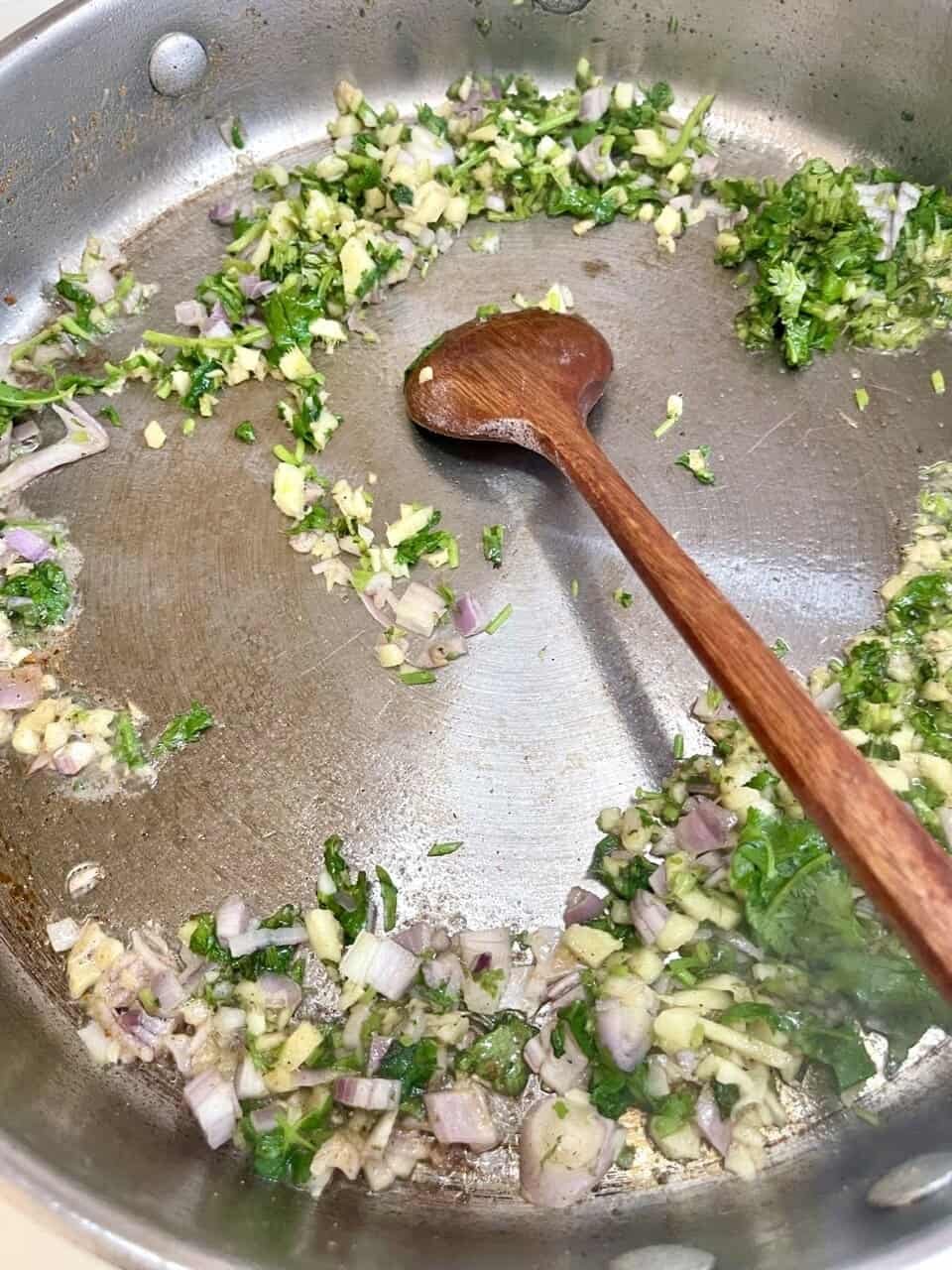 Sauteing chopped onions, garlic, and herbs in a stainless steel skillet for a flavorful base.