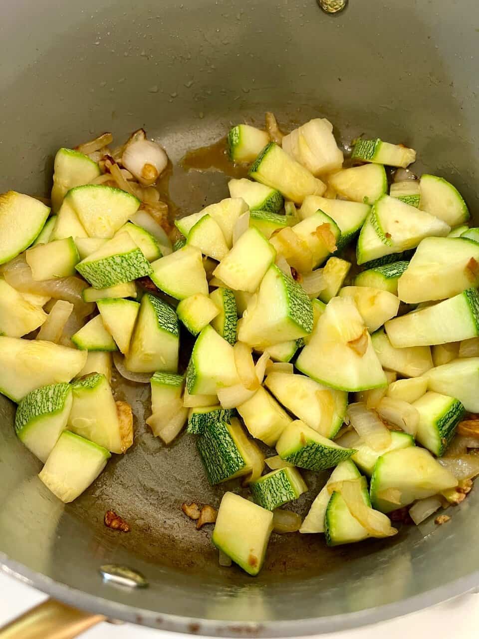 Sautéed zucchinis and onions in a cooking pan, fresh vegetable preparation for healthy meals.
