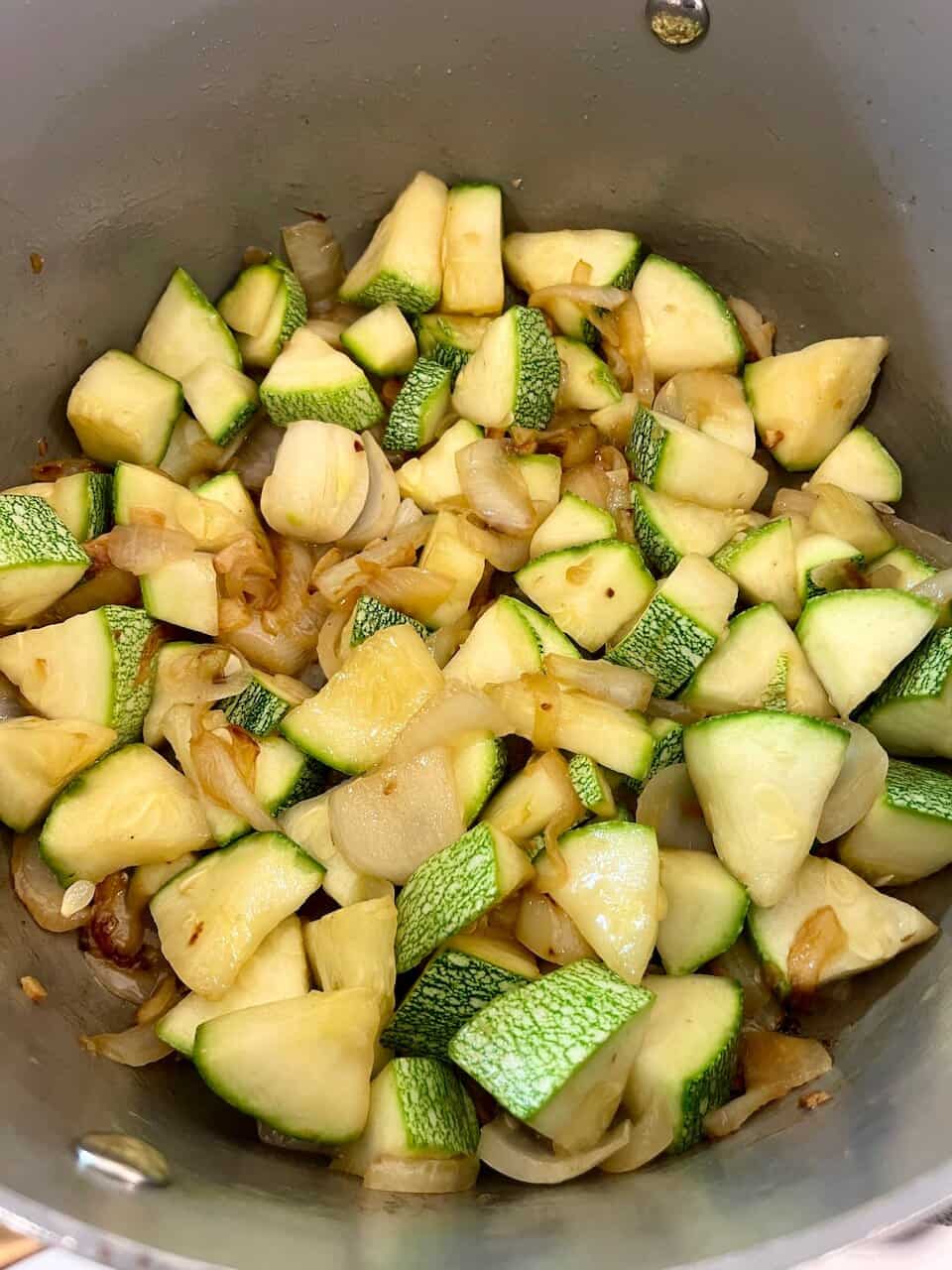Cooked zucchini and onions in a skillet, preparing a healthy plant-based meal.
