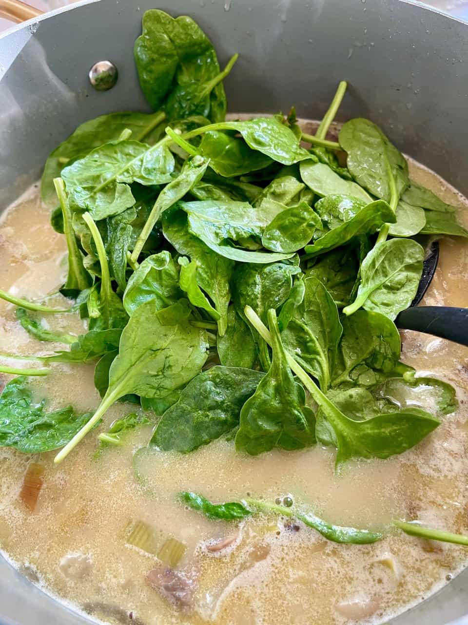 Fresh spinach leaves cooking in a creamy broth, healthy vegan meal, nutrient-rich greens, making pure thy heart.