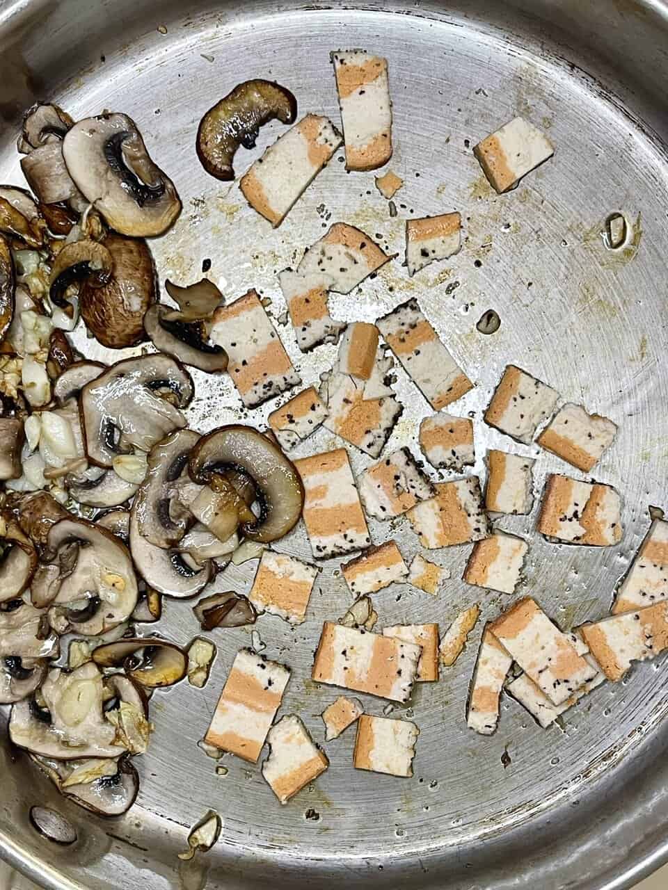 Sliced tofu and mushrooms cooking in a stainless steel pan, healthy plant-based ingredients.