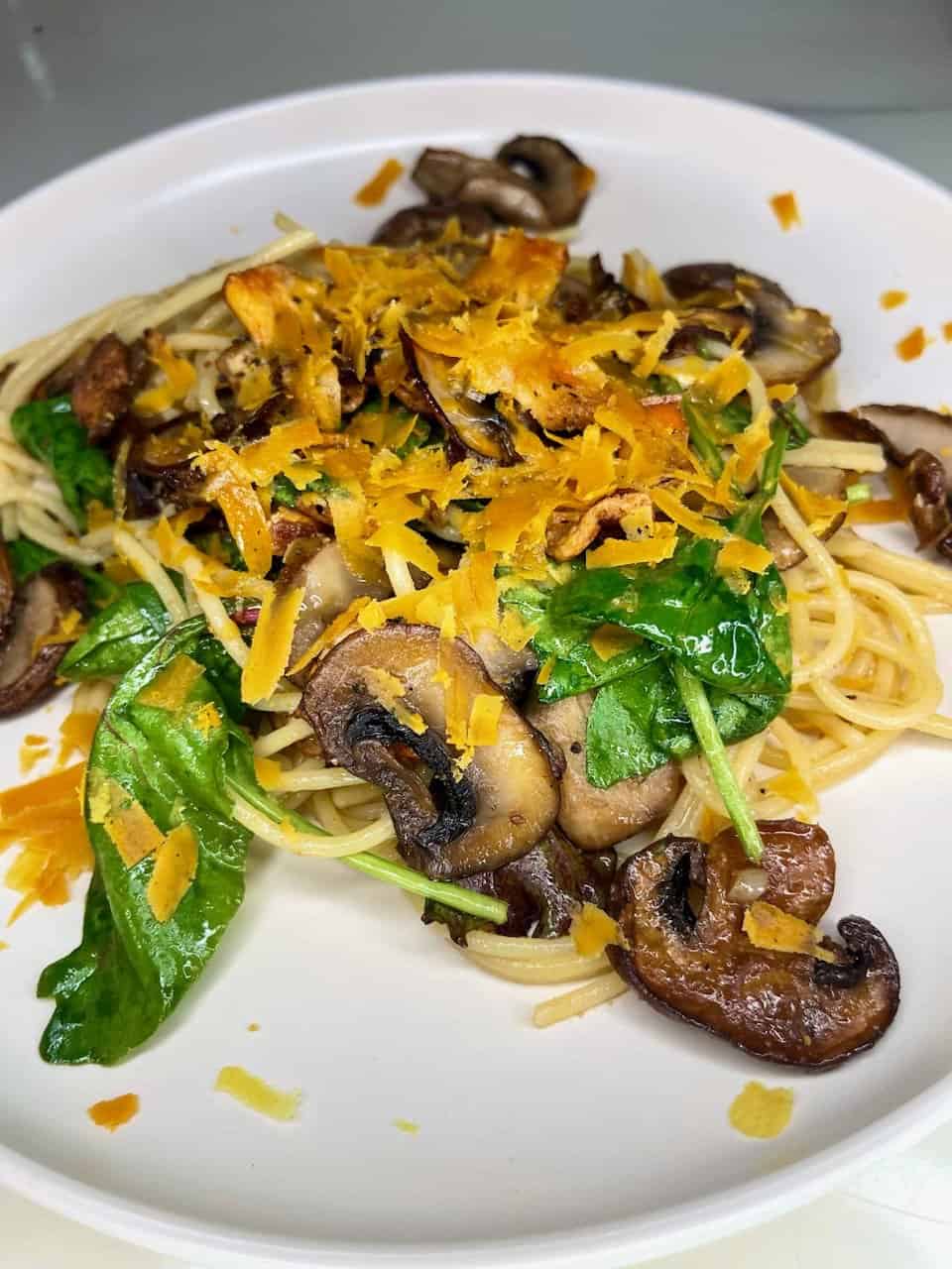 Savory mushroom spinach pasta dish with shredded cheese on a white plate, nutritious and flavorful.
