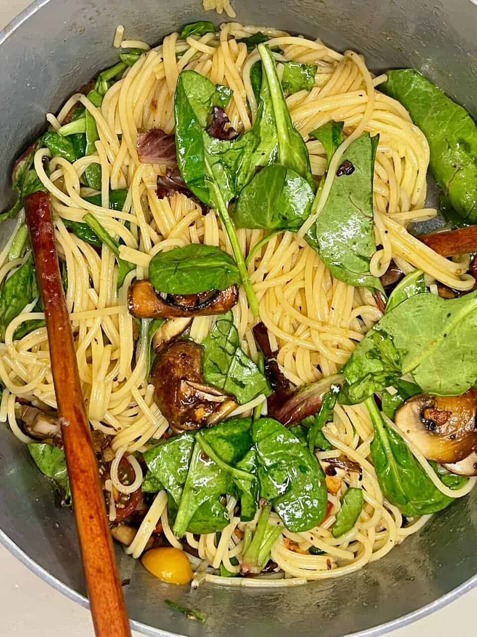 Fresh vegan pasta salad with spinach, mushrooms, cherry tomatoes, and herbs, healthy plant-based meal.