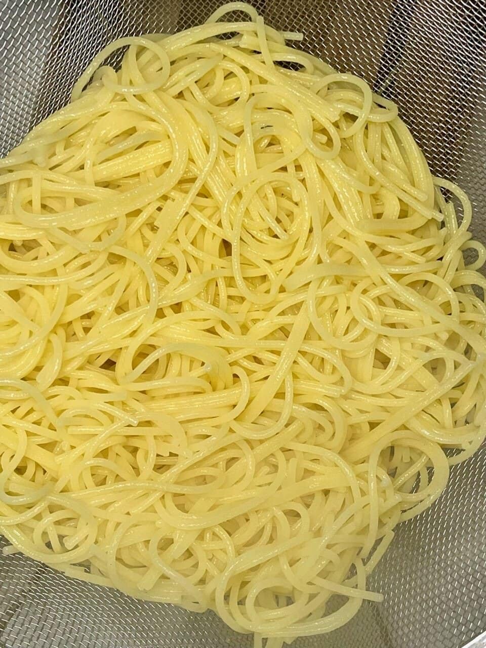 Sliced cooked spaghetti noodles in a mesh strainer for healthy pasta preparation.