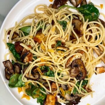 Savory mushroom and vegetable pasta with spinach and tofu on a white plate.