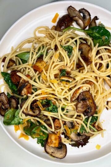 Savory mushroom and vegetable pasta with spinach and tofu on a white plate.