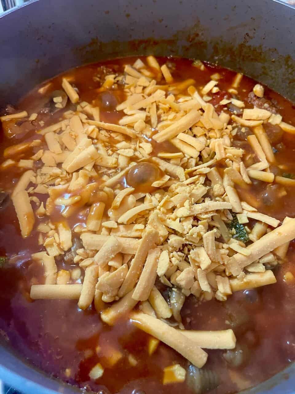 Cheesy beef & vegetable chili cooking in a pot, topped with shredded cheese for a hearty, nutritious meal.