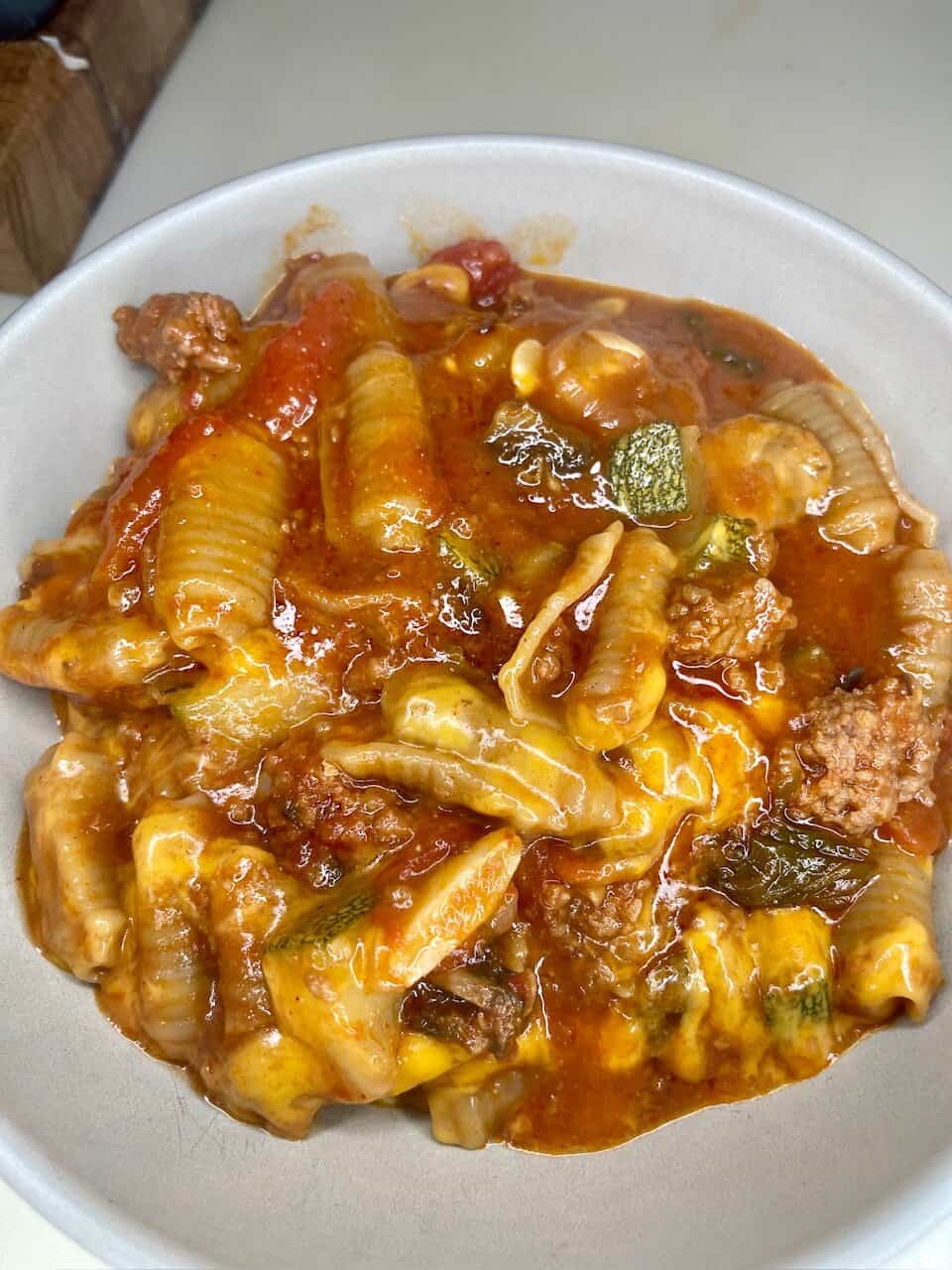 Hearty cheesy pasta with ground beef, vegetables, and tomato sauce in a disposable bowl.