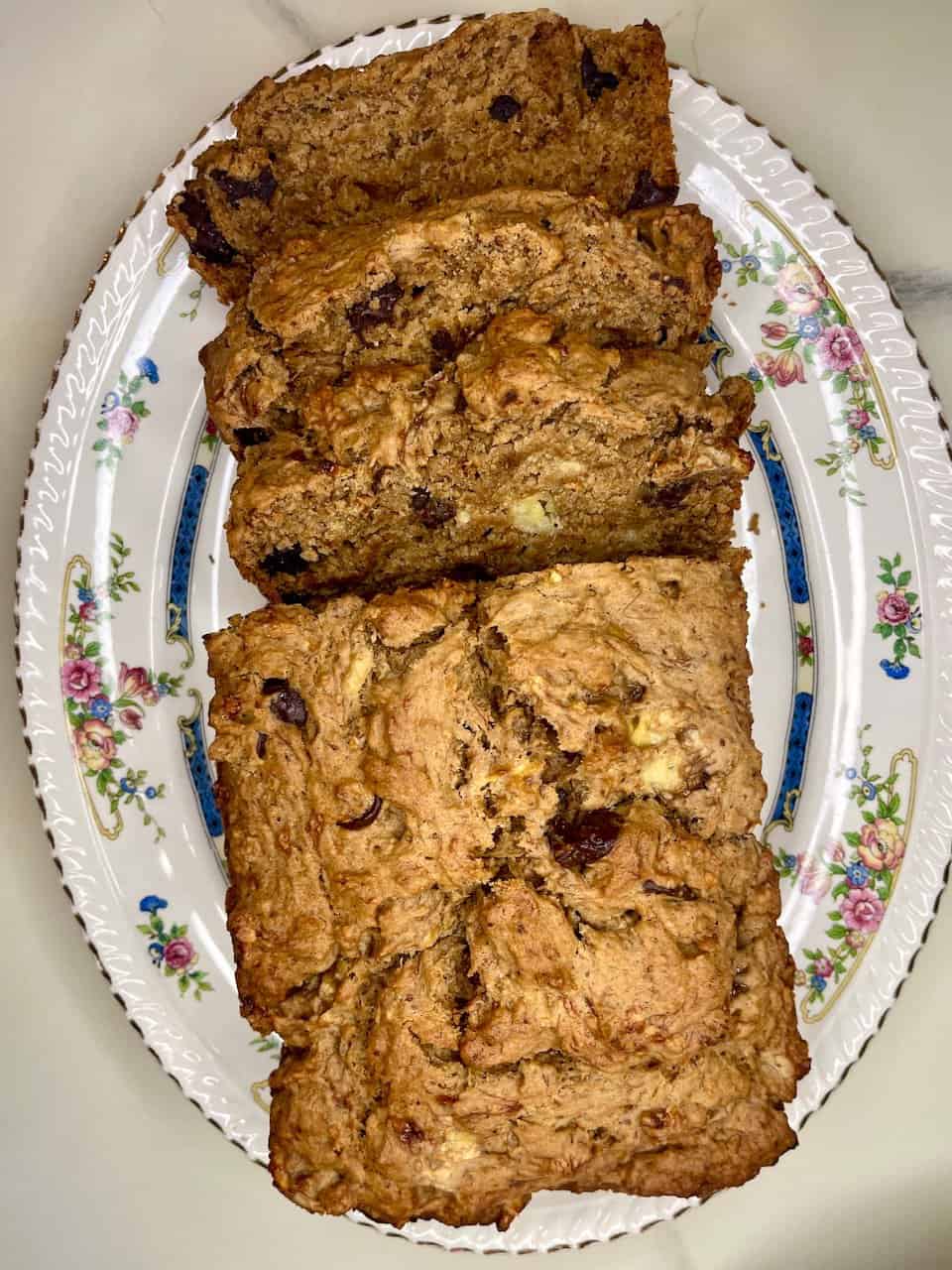 Warm chocolate chip banana bread loaf slices on floral platter for healthy baking recipes.