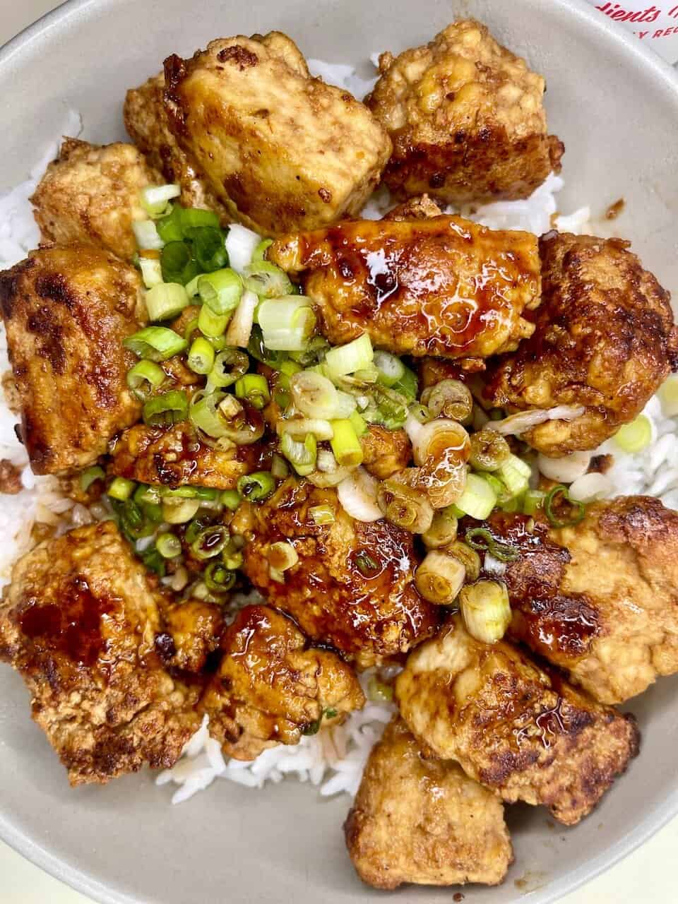 Crispy fried chicken pieces topped with savory sauce and chopped green onions on rice. Delicious comfort food with a flavorful, seasoned crust.