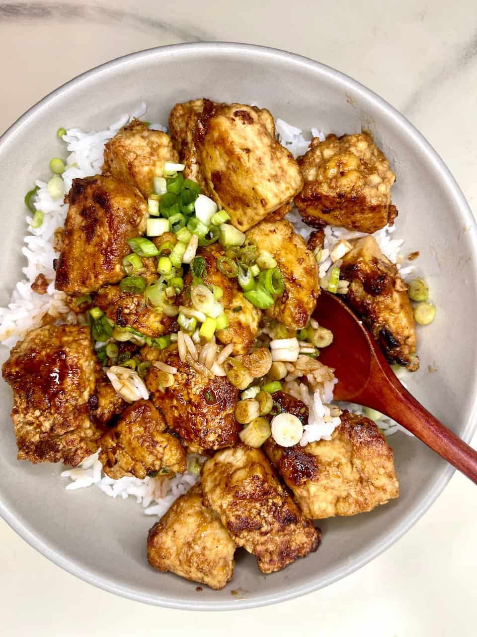 Golden fried tofu served over rice with chopped green onions and a savory sauce, creating a healthy and delicious meal.