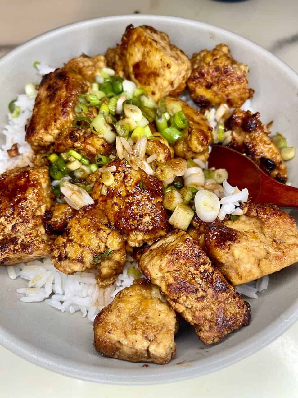 Savory crispy tofu stir-fry with green onions on white rice, healthy plant-based meal.