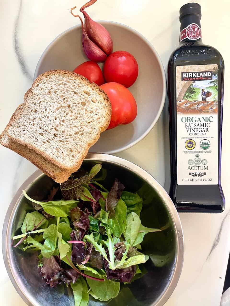 Fresh organic salad ingredients with bread, tomatoes, garlic, and balsamic vinegar for healthy eating.