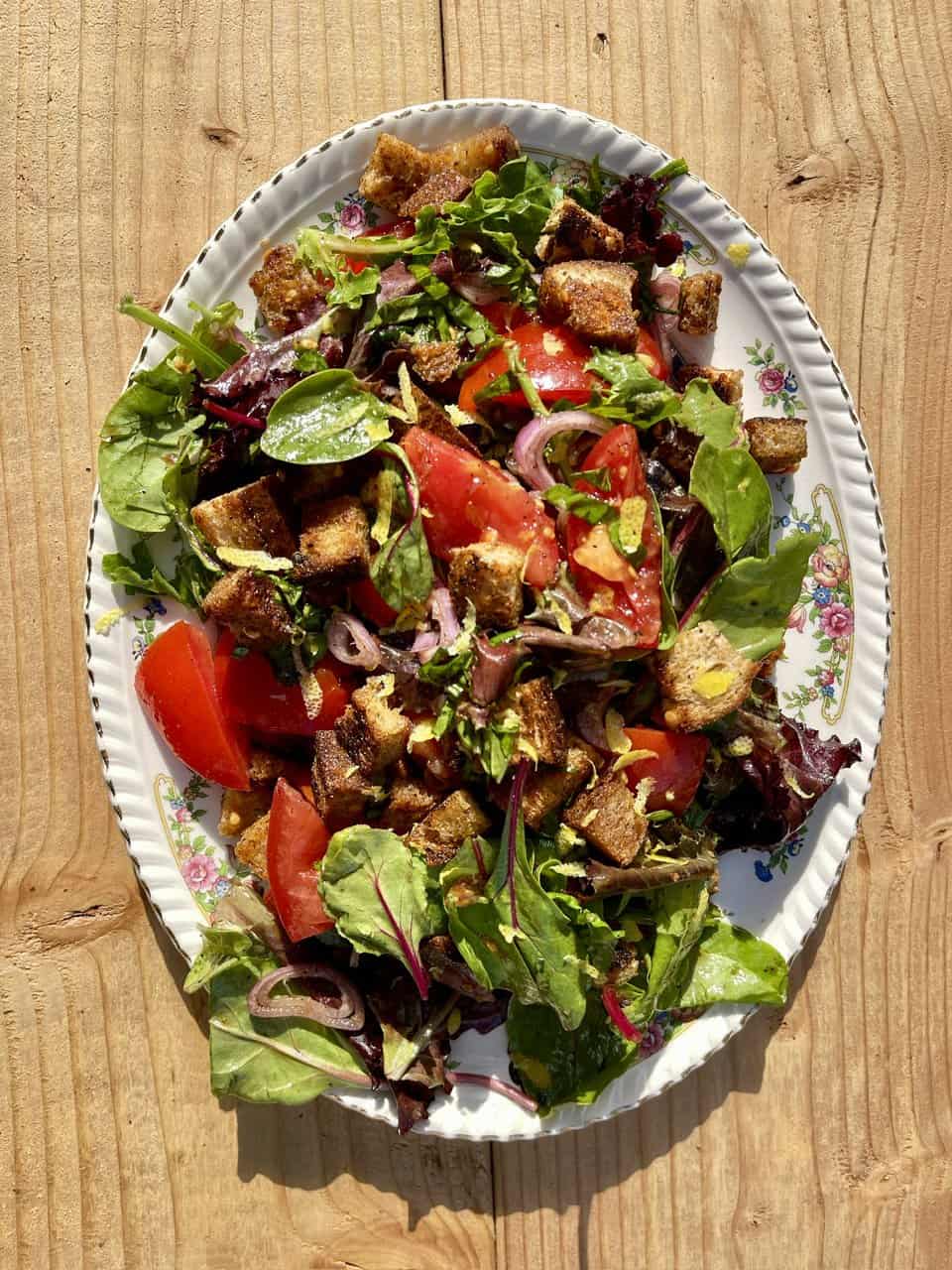 Fresh mixed green salad with tomatoes, red onions, and crispy croutons on a vintage floral platter for healthy eating.