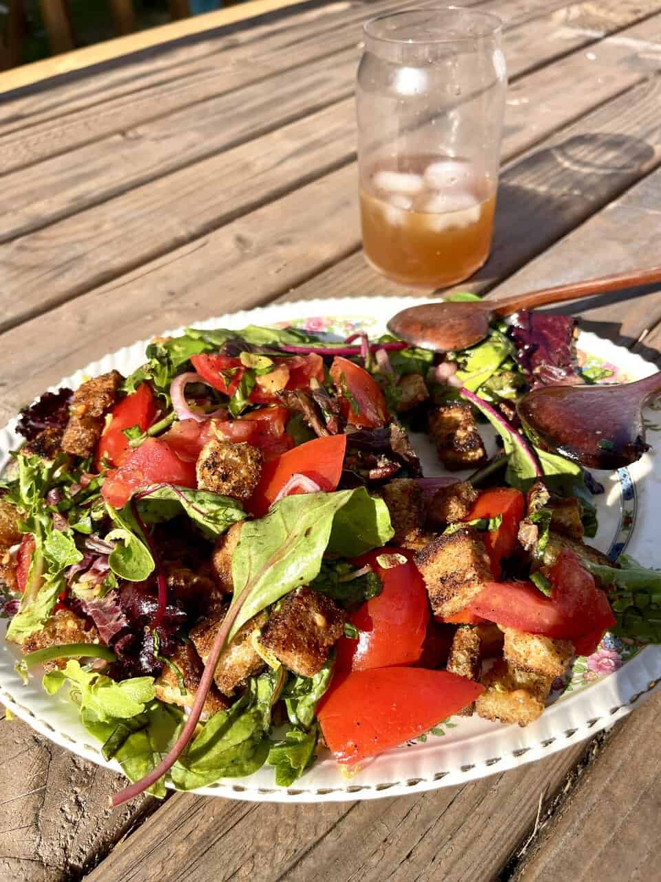 Fresh mixed greens salad with tomatoes and croutons, served outdoors with a glass of iced tea.