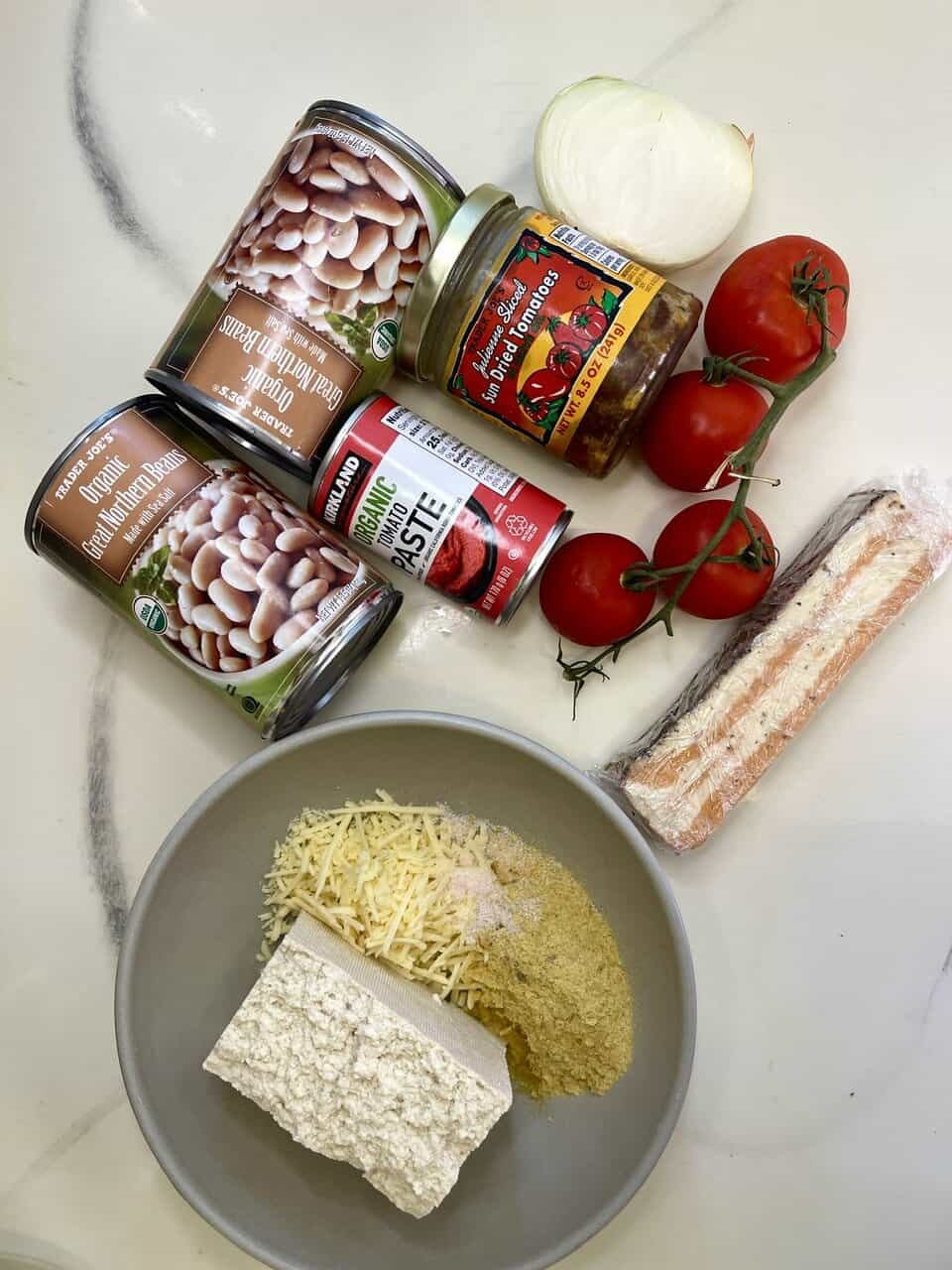 Canned organic beans, tomato, onion, plant-based cheese, tomato paste, sun-dried tomatoes, plant-based Parmesan, and crushed plant-based protein in bowl, promoting healthy eating and plant-based cooking.
