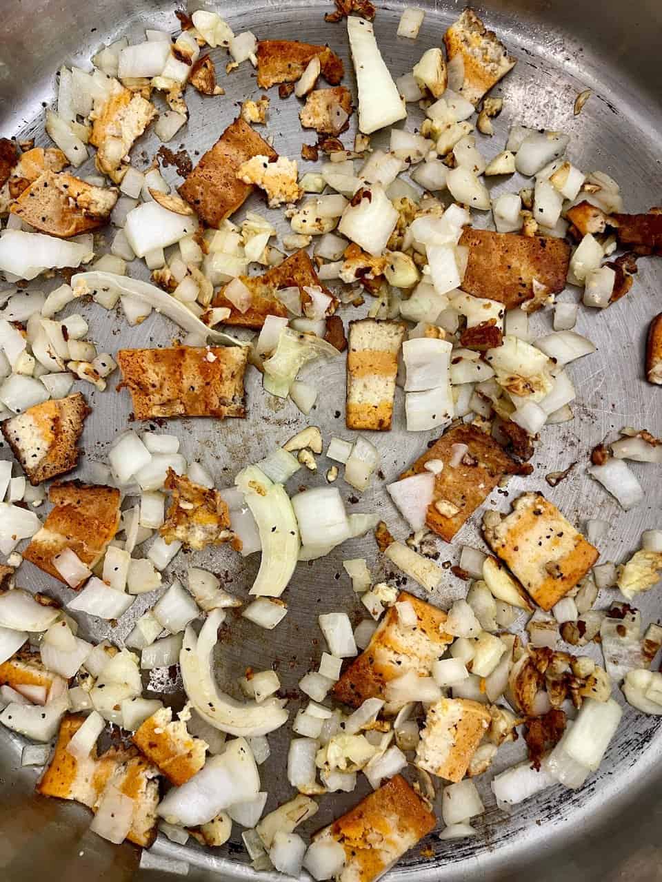 Crispy fried tofu with sautéed onions in a skillet healthy vegan protein source.