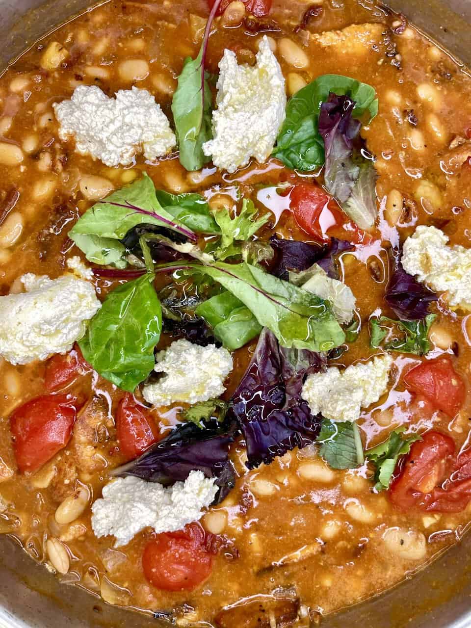 Fresh vegetable soup with beans and cheese, vibrant salad greens topping, healthy and hearty meal.