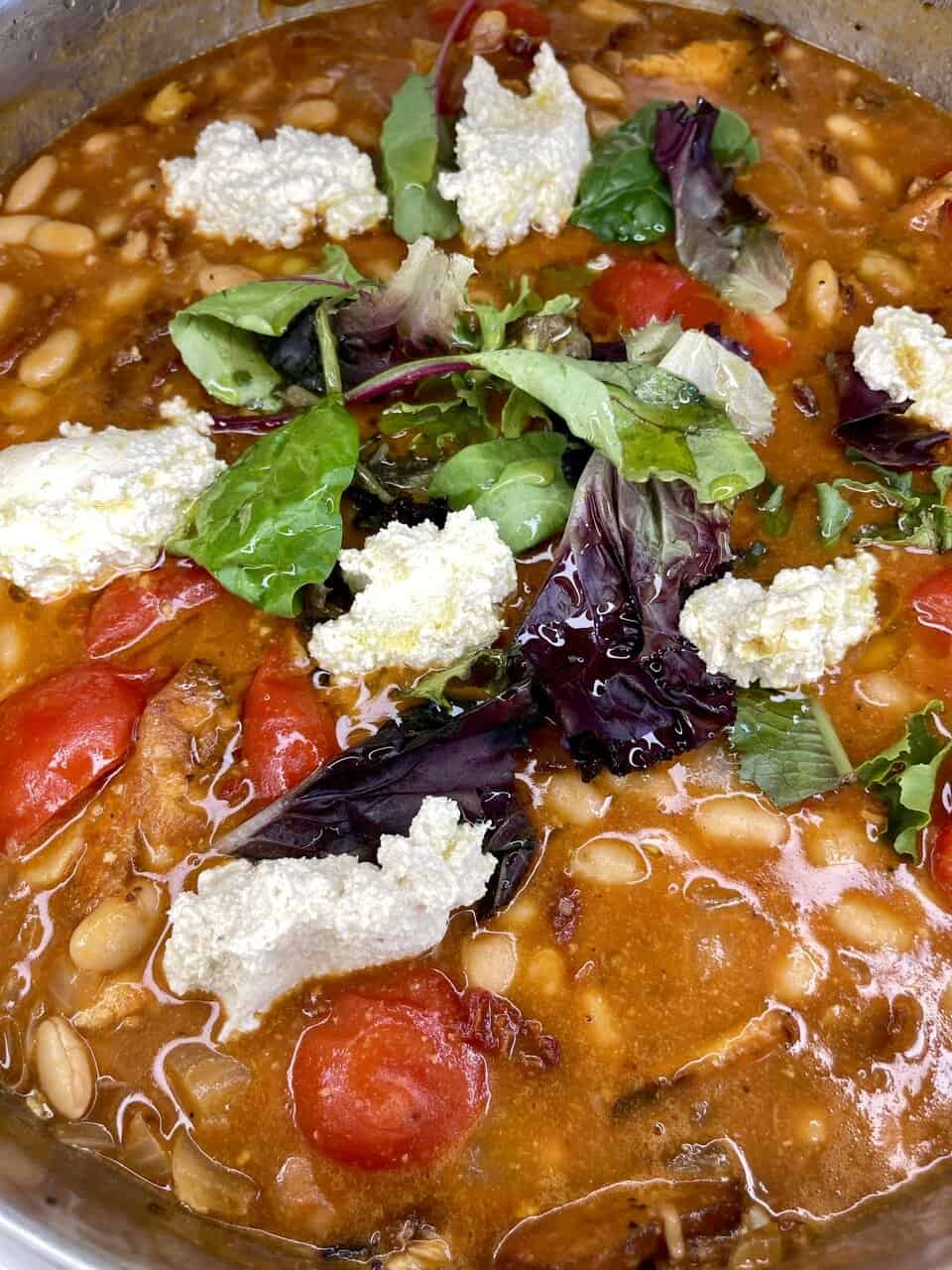 Vegetarian bean soup with fresh mixed greens, cherry tomatoes, and dollops of ricotta cheese.