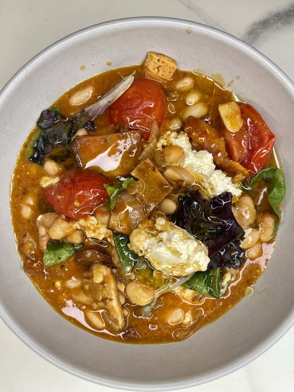 Fresh vegetable and bean soup with tomatoes, greens, tofu, and herbs, promoting healthy eating and wellness.