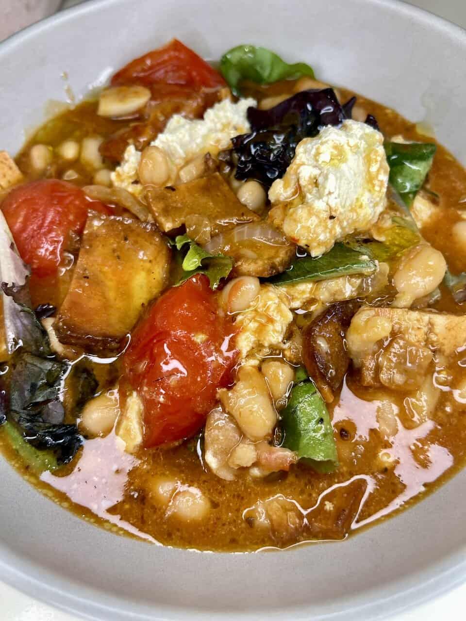 Savory vegetable curry with tomatoes, greens, tofu, and beans, served in a flavorful broth.