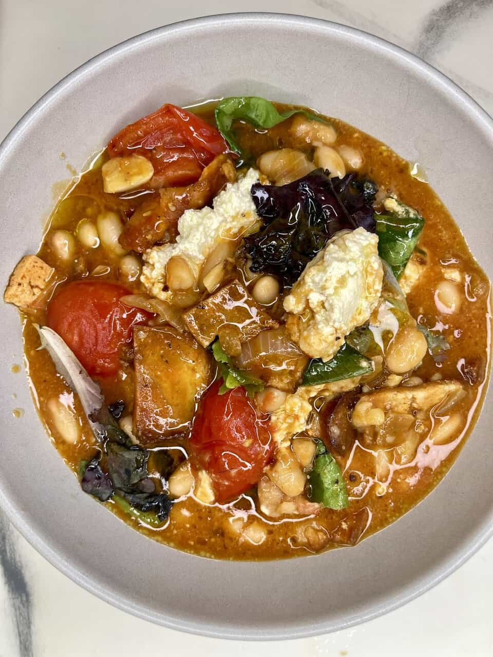 Vegan vegetable soup with beans, tomatoes, greens, and tofu in a rustic bowl.