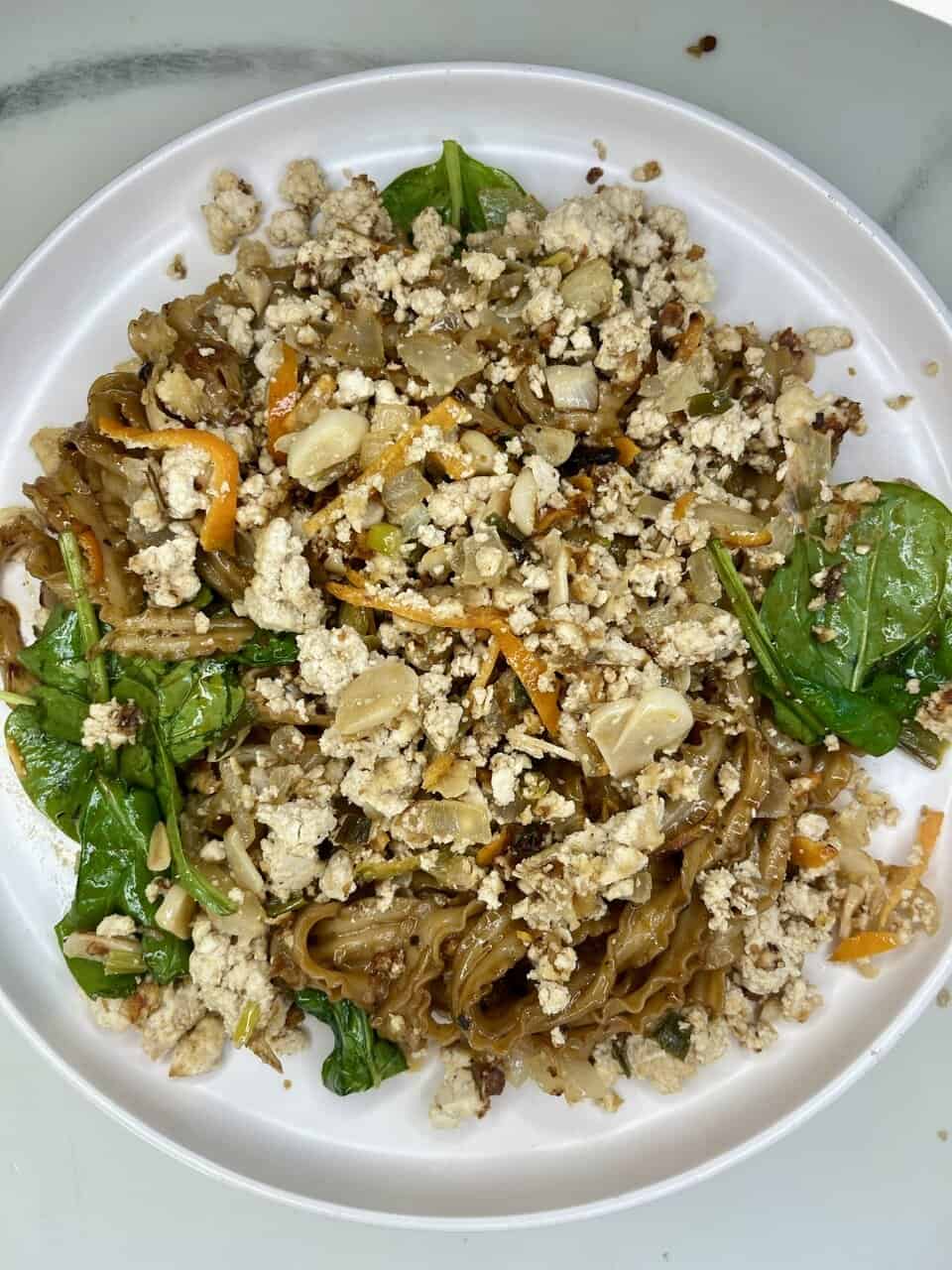 Savory gluten-free plant-based vegetable and tofu stir-fry with noodles and fresh greens.