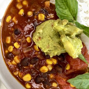 Savory black bean and corn chili with avocado and rice, healthy vegan meal, fresh basil garnish.