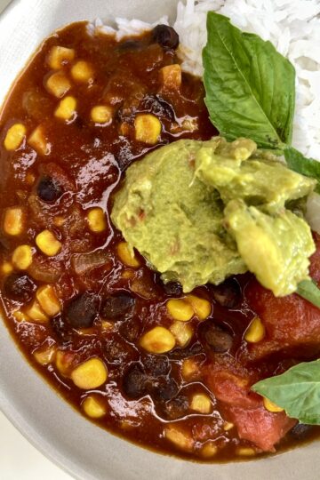 Savory black bean and corn chili with avocado and rice, healthy vegan meal, fresh basil garnish.