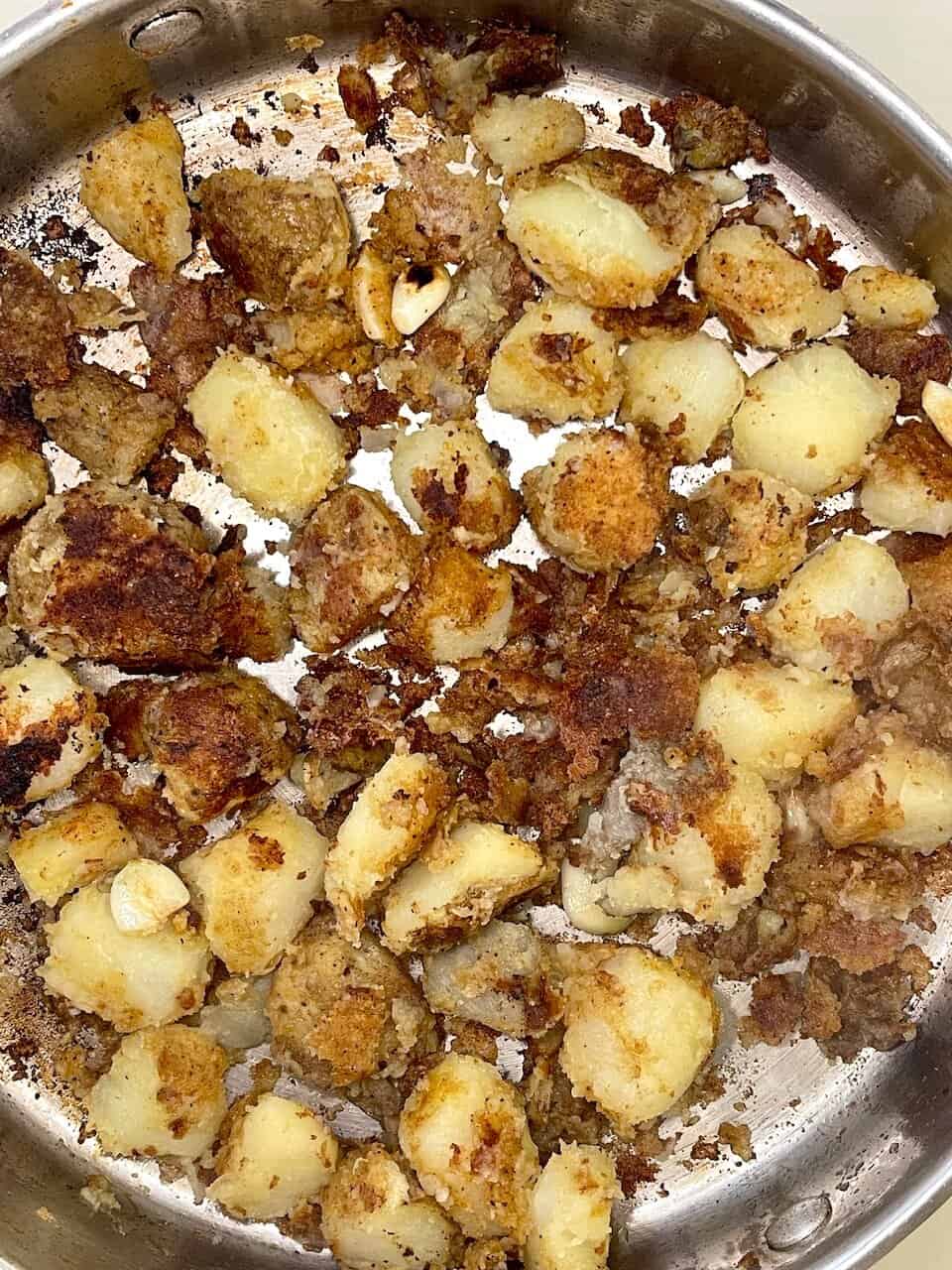 Gelatinous potatoes roasted with spices and garlic in a stainless steel pan.