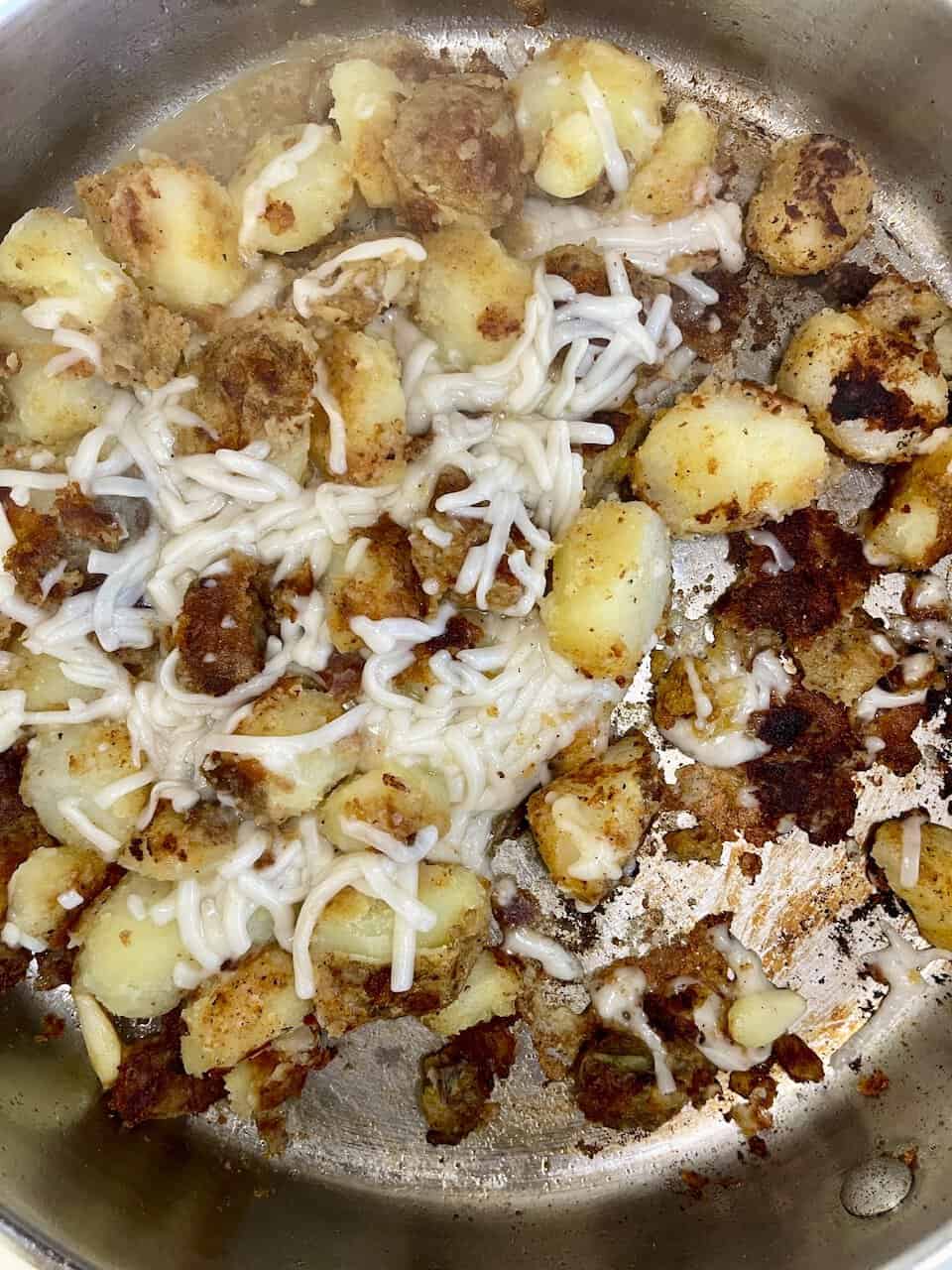 Crispy roasted potatoes with melted cheese in a skillet, savory comfort food, vegetarian friendly,meaty texture, golden brown edges, delicious homemade meal.