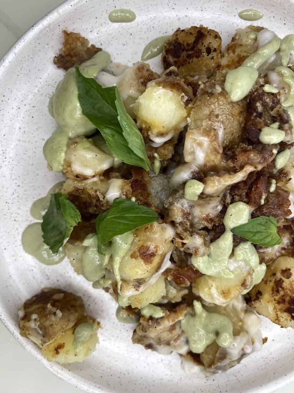 Crispy potato bites with creamy herb sauce and fresh basil leaves on a white plate.