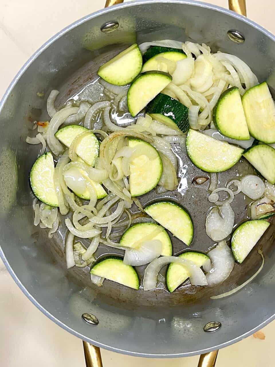 Cooking zucchini and onions in a pan for healthy meals.