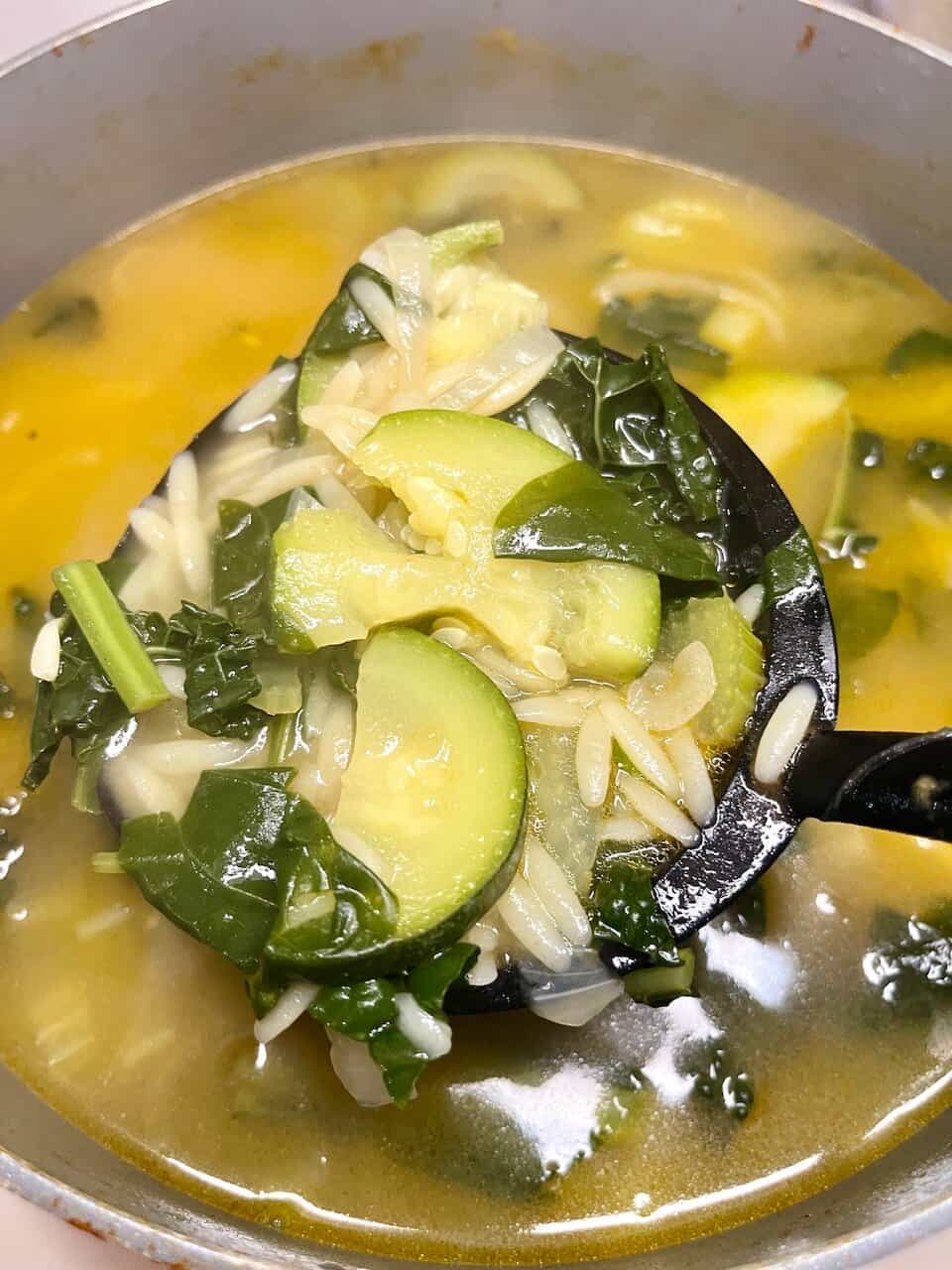 Fresh vegetable soup with zucchini, leafy greens, and orzo pasta. Healthy, comforting homemade meal.