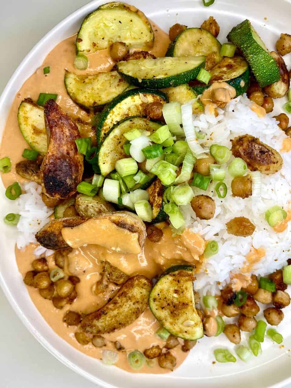 Grilled zucchini and chickpea plant-based meal with creamy peanut sauce, rice, and fresh green onions.