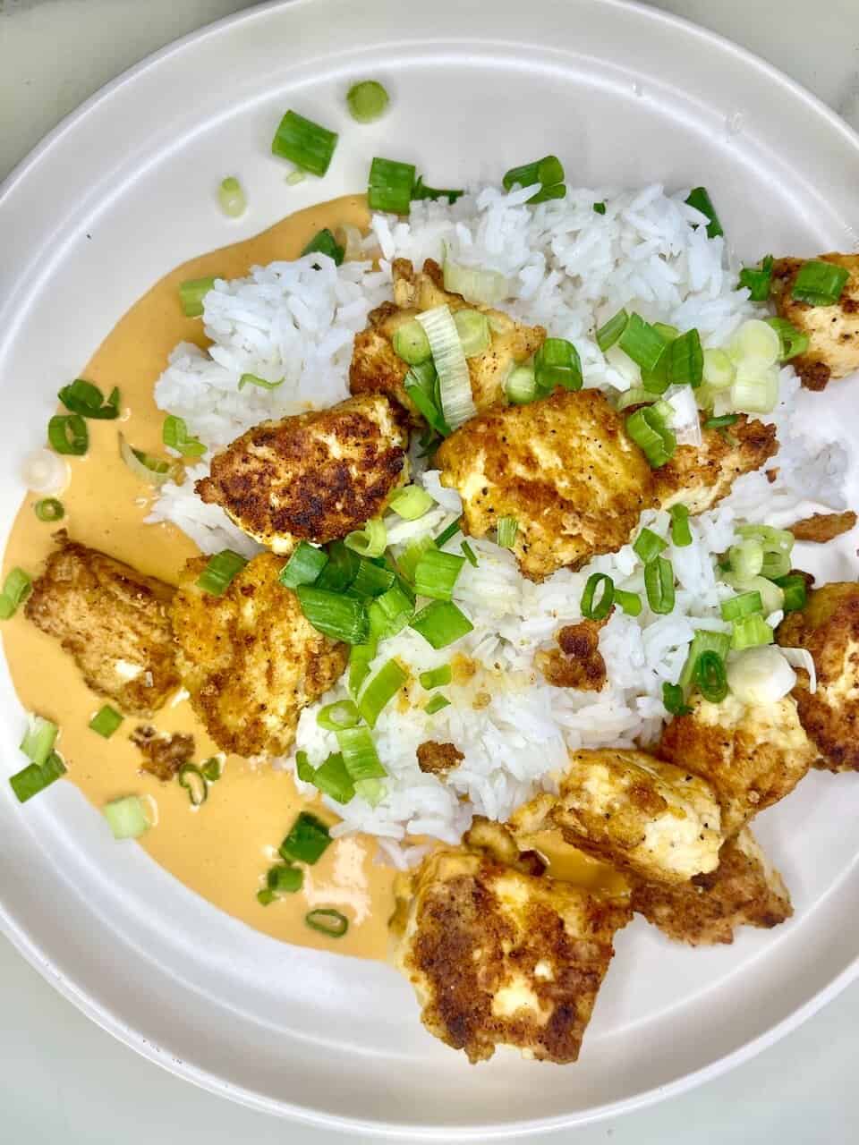 Crispy fried chicken with white rice and green onion on a white plate, drizzled with creamy sauce.