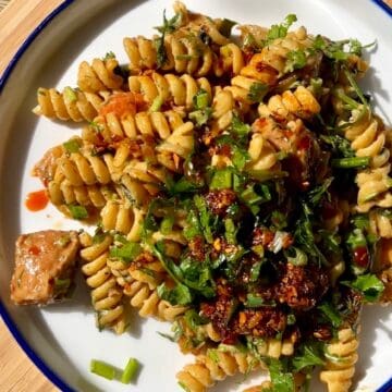 Spicy pasta with fusilli, greens, and chili flakes on a white plate.