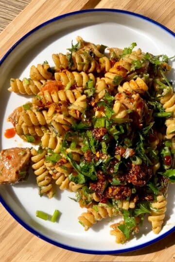 Spicy pasta with fusilli, greens, and chili flakes on a white plate.