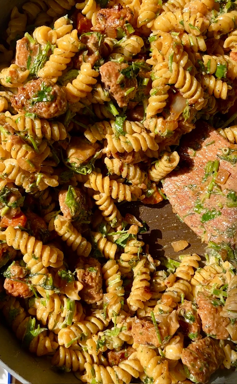 Spicy pasta with sausage, herbs, and sauce in a skillet.